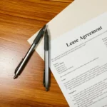 Dokumen perjanjian sewa atau lease di atas meja kayu dengan dua pena, menggambarkan kontrak lease bisnis